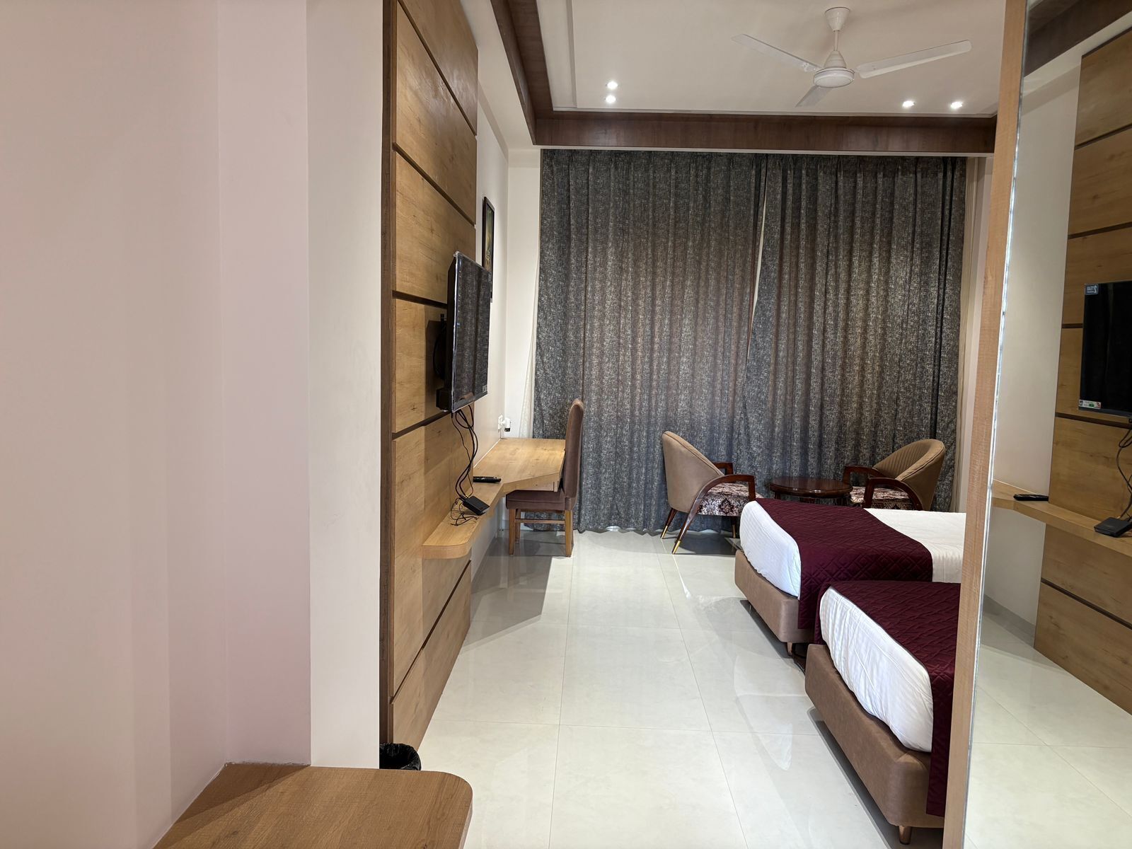 A modern hotel room with two beds, a desk, a chair, a TV, and a curtain.