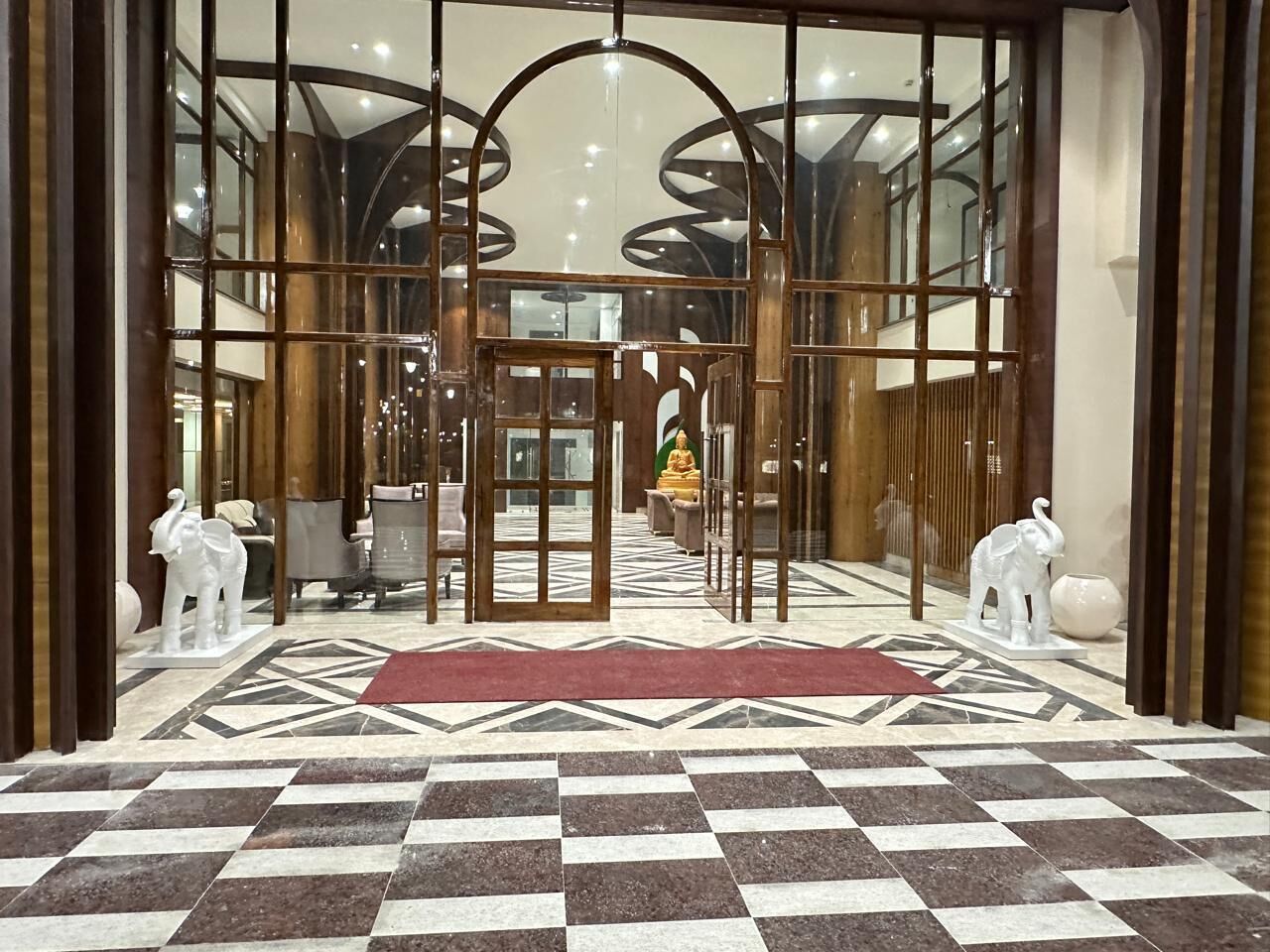 A hotel entrance with a checkered floor, a Buddha statue, and two elephant statues.