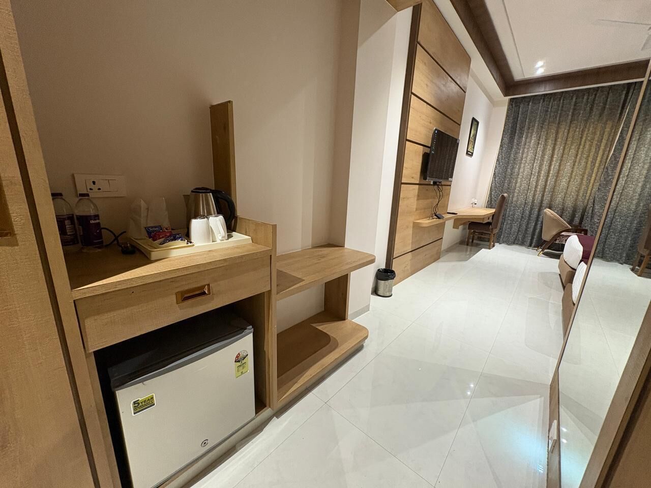 Quarto de hotel moderno com escrivaninha de madeira, mini-frigorífico, televisão de tela plana e uma grande janela com cortinas.