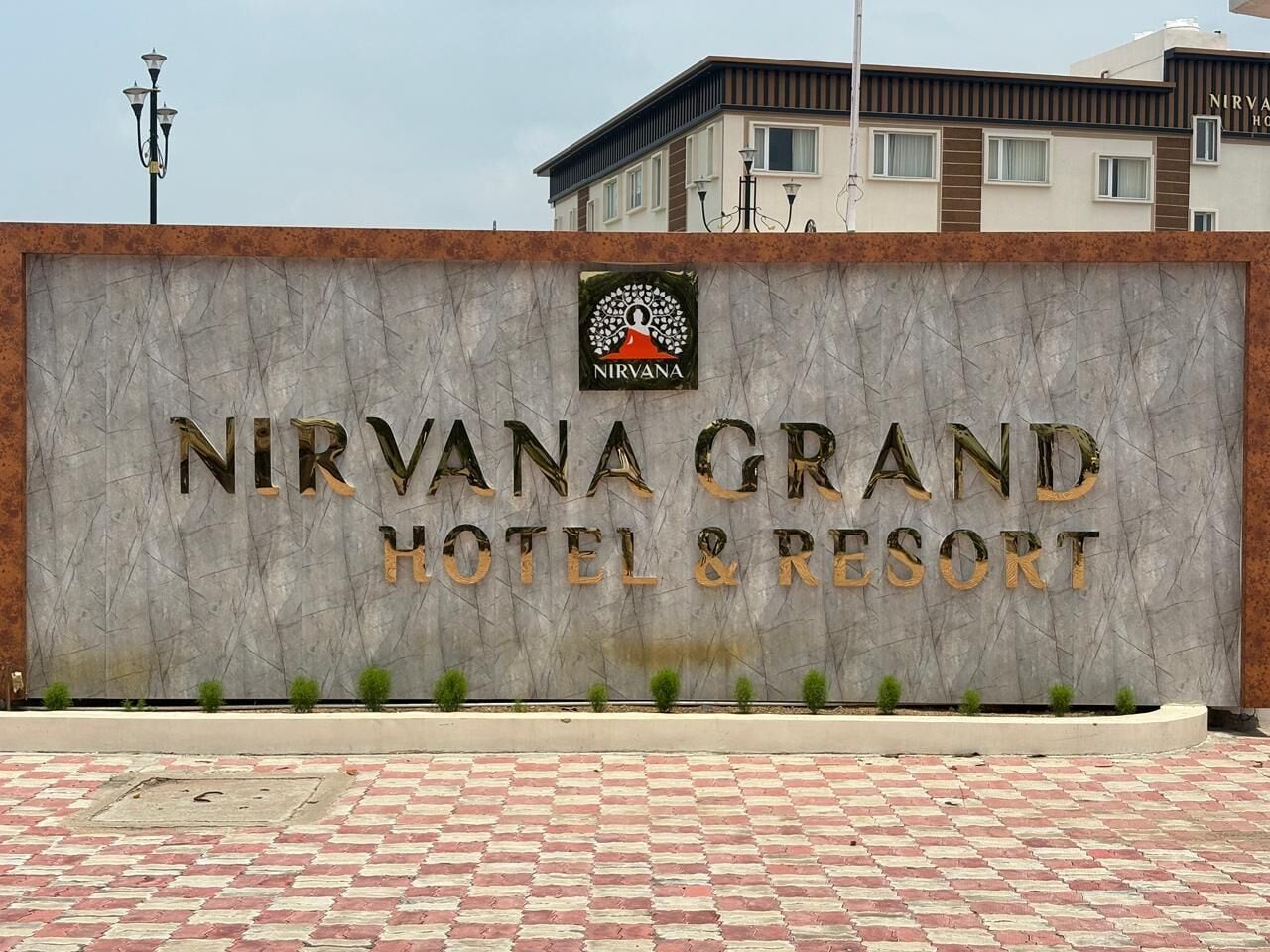 Een bord van Nirvana Grand Hotel & Resort met een marmeren gevel en een logo boven de naam.