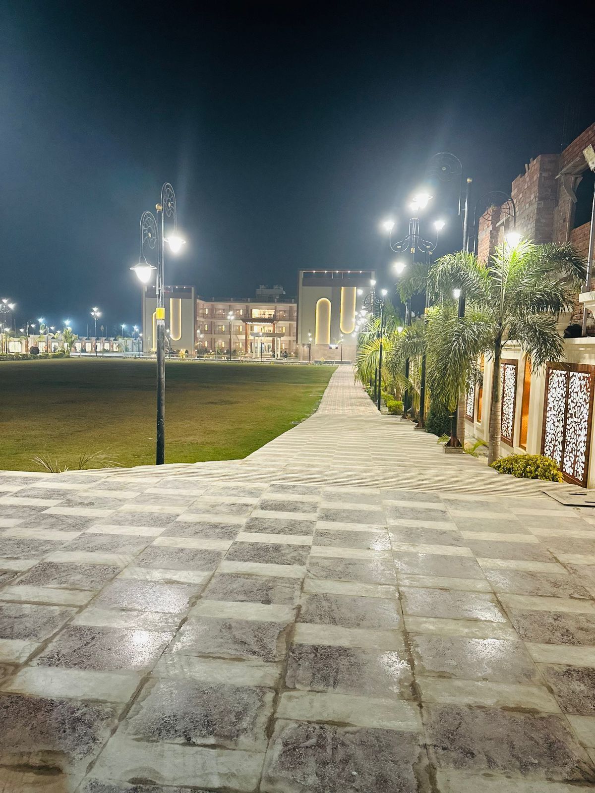 A paved pathway leading to a building with a modern design, featuring a large arched entrance and a well-lit facade.