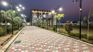 Un sendero pavimentado que conduce a un edificio con múltiples luminarias y palmeras.