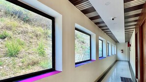 A corridor with large windows, a polished floor, and a wooden ceiling. - Dhurva Hotel and Resort (Lansdowne)