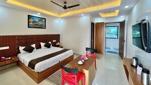 A modern hotel room with a wooden bed, a desk with a chair, a television, and a ceiling fan. - Dhurva Hotel and Resort (Lansdowne)
