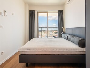 A modern bedroom with a large bed, a view of a cityscape through a large window, and a balcony. - Central Apartment in Ostend Near Beach (Ostend)
