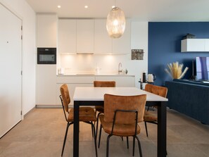 A modern kitchen with white cabinets, a dining table with chairs, and a hanging pendant light. - Central Apartment in Ostend Near Beach (Ostend)