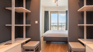 A bedroom with a bed, two bedside tables, a wardrobe, and a window with a city view. - Central Apartment in Ostend Near Beach (Ostend)