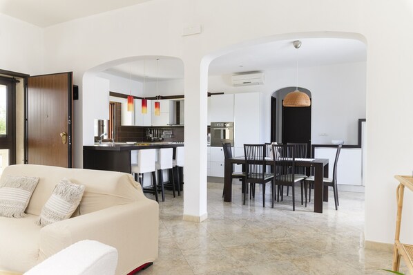 A modern living room with a sofa and a dining area with chairs and a table. - Villa Alexander con Piscina by Wonderful Italy (San Vito dei Normanni)