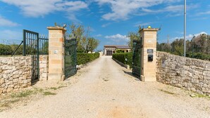 A gravel driveway leading to a gated entrance with stone walls and a building in the background. - Villa Alexander con Piscina by Wonderful Italy (San Vito dei Normanni)