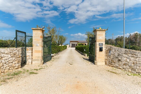 A gravel driveway leading to a gated entrance with stone walls and a building in the background. - Villa Alexander con Piscina by Wonderful Italy (San Vito dei Normanni)