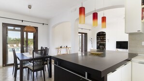 A modern kitchen with a large island, pendant lights, and a dining area with a view of the outdoors. - Villa Alexander con Piscina by Wonderful Italy (San Vito dei Normanni)