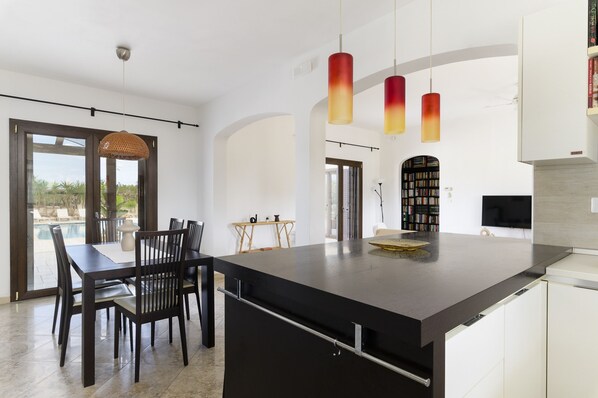 A modern kitchen with a large island, pendant lights, and a dining area with a view of the outdoors. - Villa Alexander con Piscina by Wonderful Italy (San Vito dei Normanni)