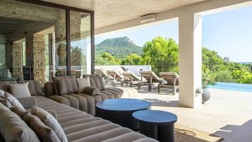 Un espacio exterior moderno con un sofá grande, dos mesas redondas y sillones de descanso.