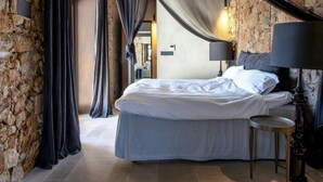 A bedroom with a bed, curtains, a lamp, and a stone wall.
