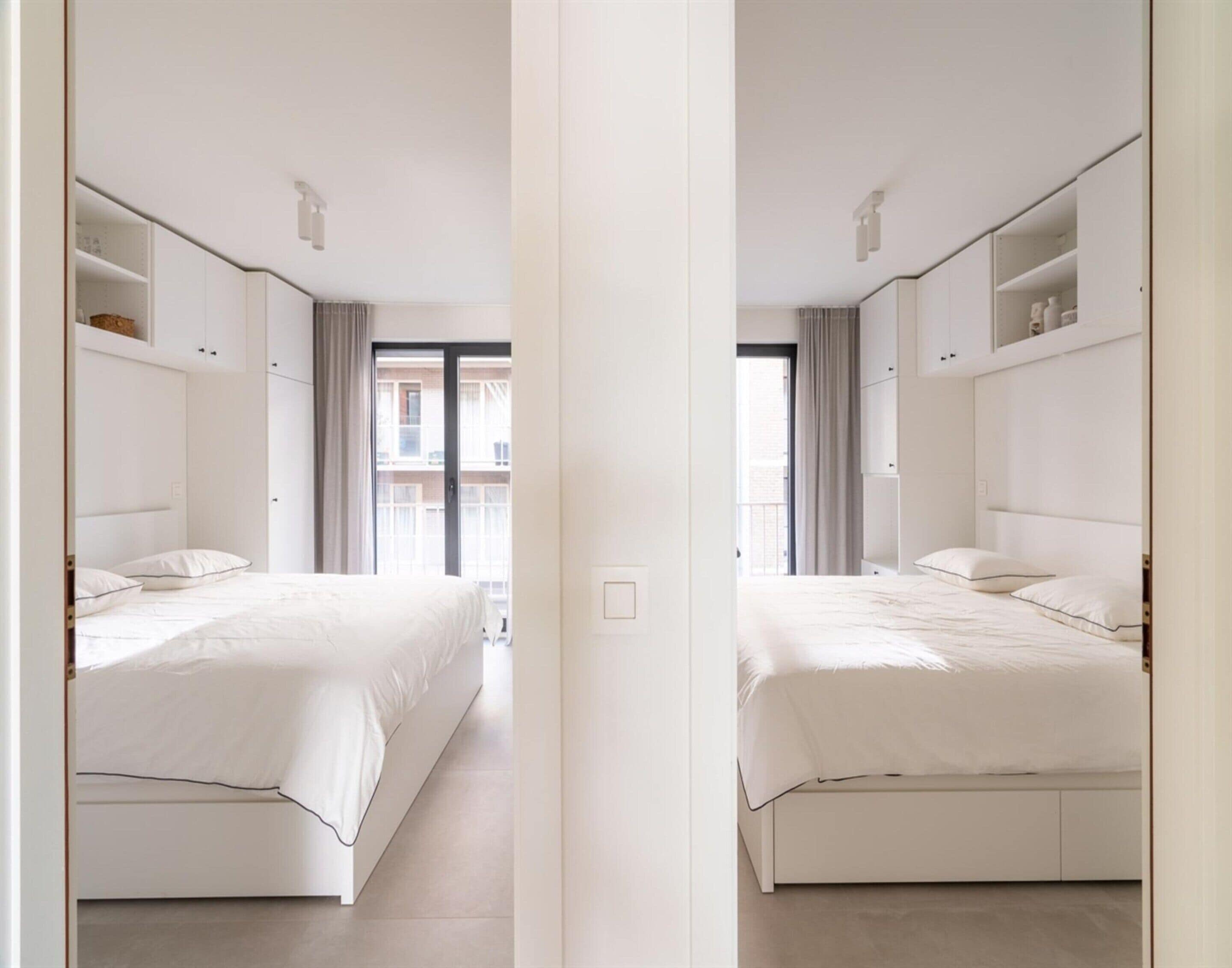 A mirrored view of a hotel room with two beds, built-in wardrobes, and a view of the outside.
