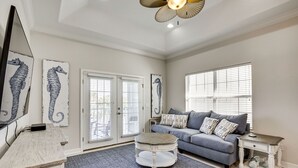 Un salon avec un canapé gris, une table basse et un tapis. Il y a deux portes et une fenêtre avec des stores.