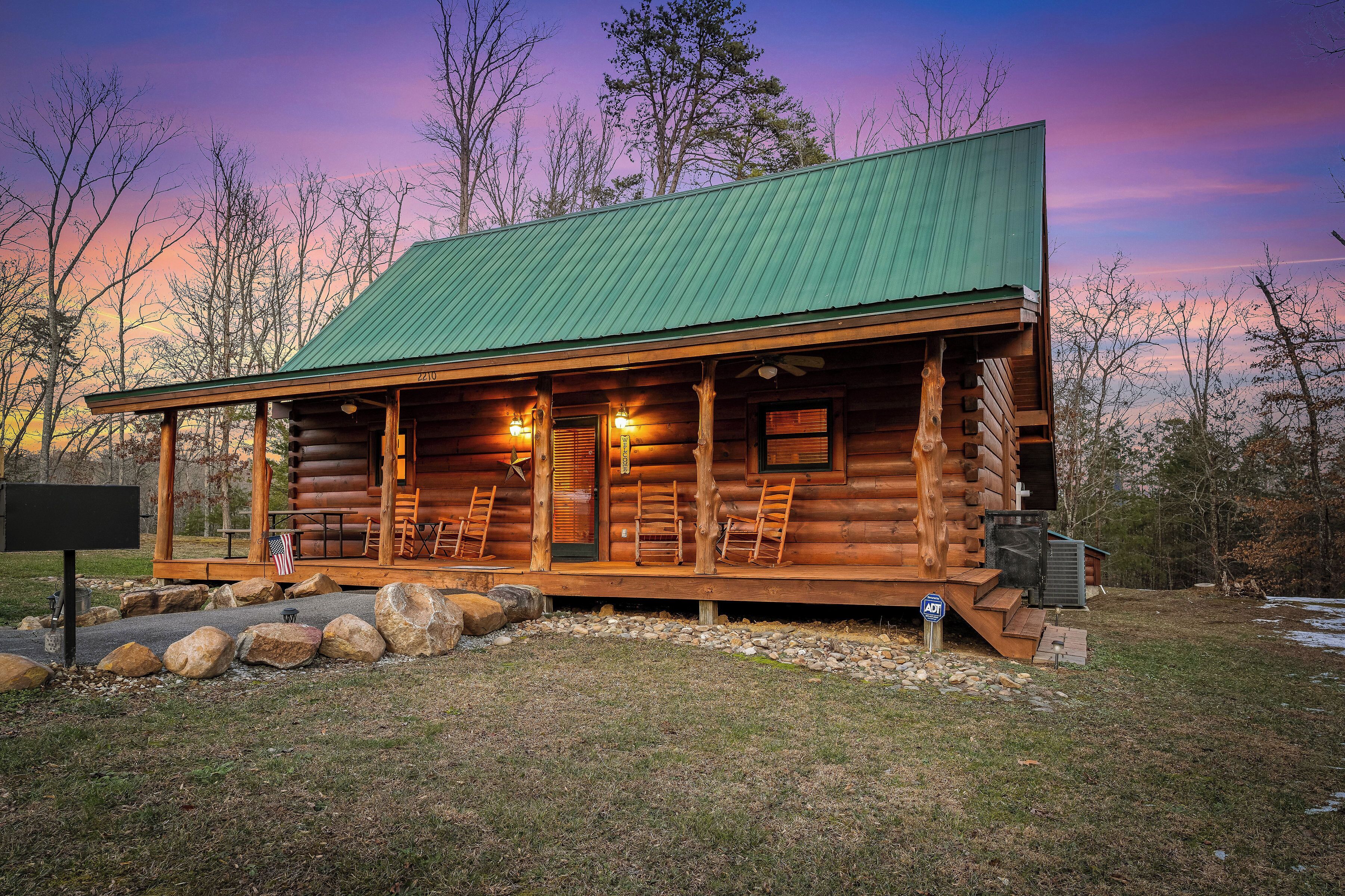 A log cabin with a green roof, wooden porch, and a flag.