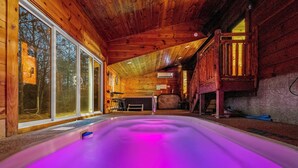 A wooden cabin with a hot tub, large windows, and a loft area. - Dog Friendly! Private Indoor Pool, Hot Tub, GameRoom, Firepit & Free Passes. (Sevierville)