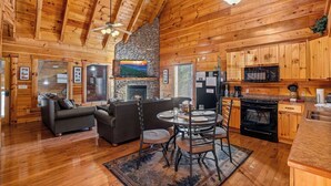 A log cabin interior with a fireplace, dining area, kitchen, and a stone wall. - Dog Friendly! Private Indoor Pool, Hot Tub, GameRoom, Firepit & Free Passes. (Sevierville)