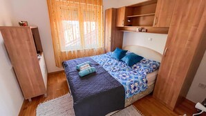 Ein kleines Schlafzimmer mit Bett, Nachttisch, Kleiderschrank und einem Fenster mit Vorhängen.