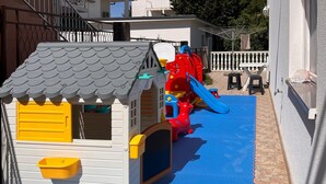 Ein Spielbereich für Kinder mit einem kleinen Haus, einer Rutsche und einem roten Spielzeugtier.
