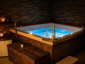 Ein Whirlpool mit Champagnerflasche und Gläsern, umgeben von Holzmöbeln und Steinwänden.