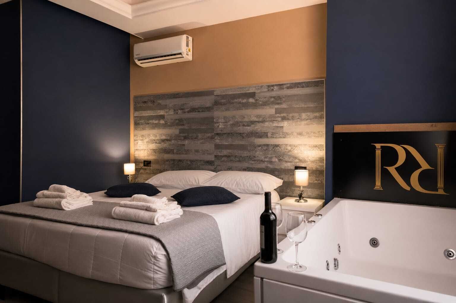 A hotel room with a bed, two bedside lamps, a bottle of wine, a glass, and a bathtub.