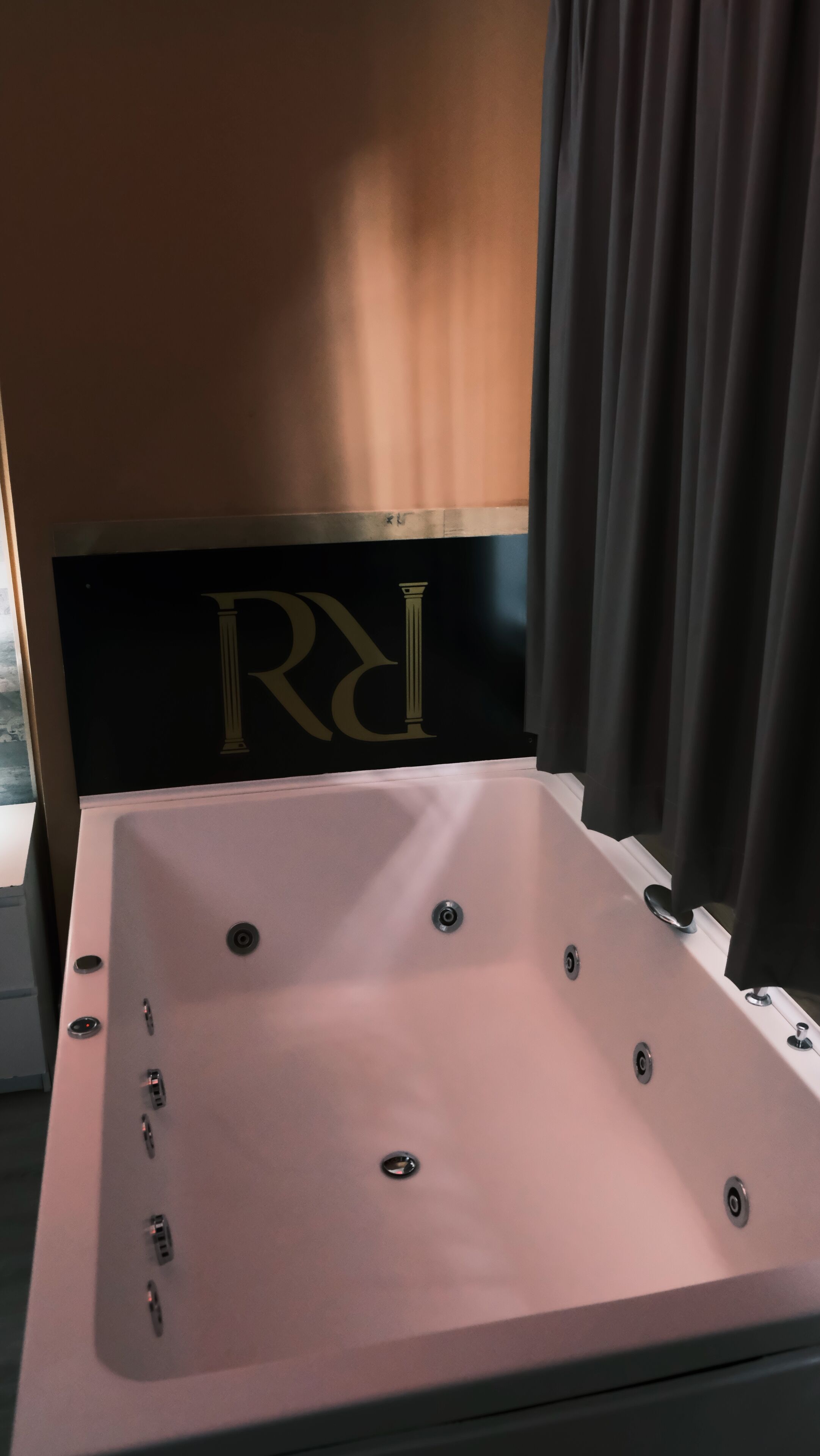 Una bañera grande y vacía con un cabecero oscuro que presenta una 'R' grande y una columna.