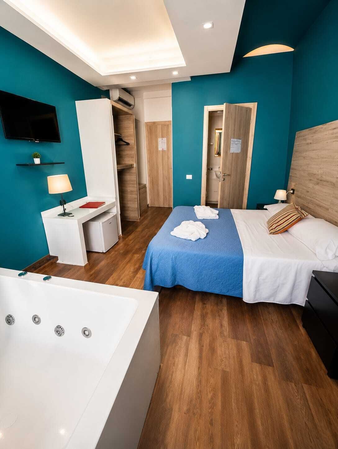 A hotel room with a bed, a desk, a chair, a TV, a bathroom, and a wardrobe.