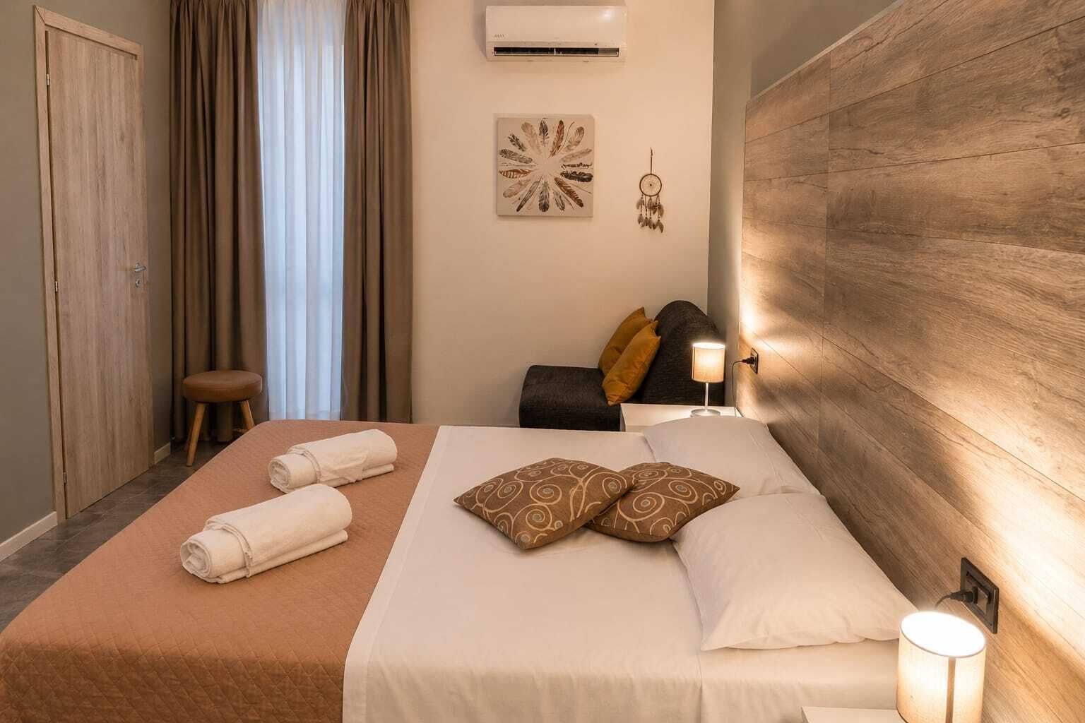 Een hotelkamer met een bed, nachtkastje, een wandairconditioner en een raam met gordijnen.