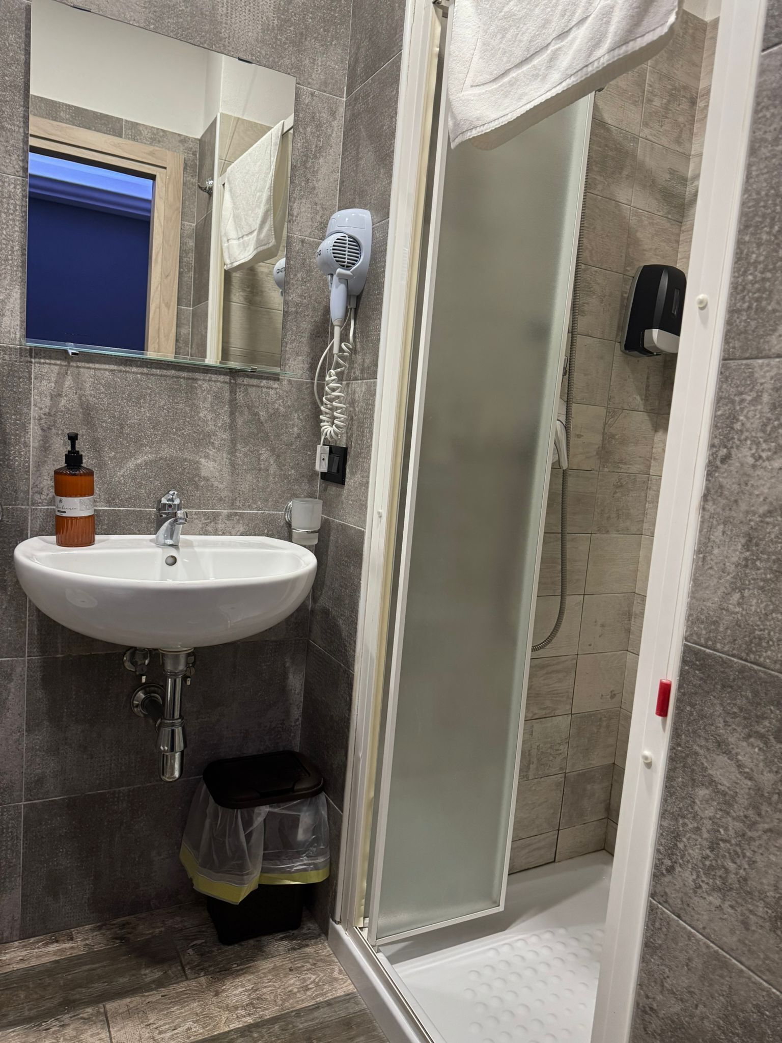 A bathroom with a white sink, a mirror, a hairdryer, and a shower area.