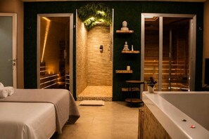 A spa room with a wooden wall, a small wooden table, a bathtub, and a bed with a towel. - Royalty room spa (Naples)