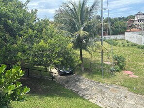 A paved pathway leading to a parked car, surrounded by lush greenery and a palm tree. - Colonial mansion (Armação dos Buzios)