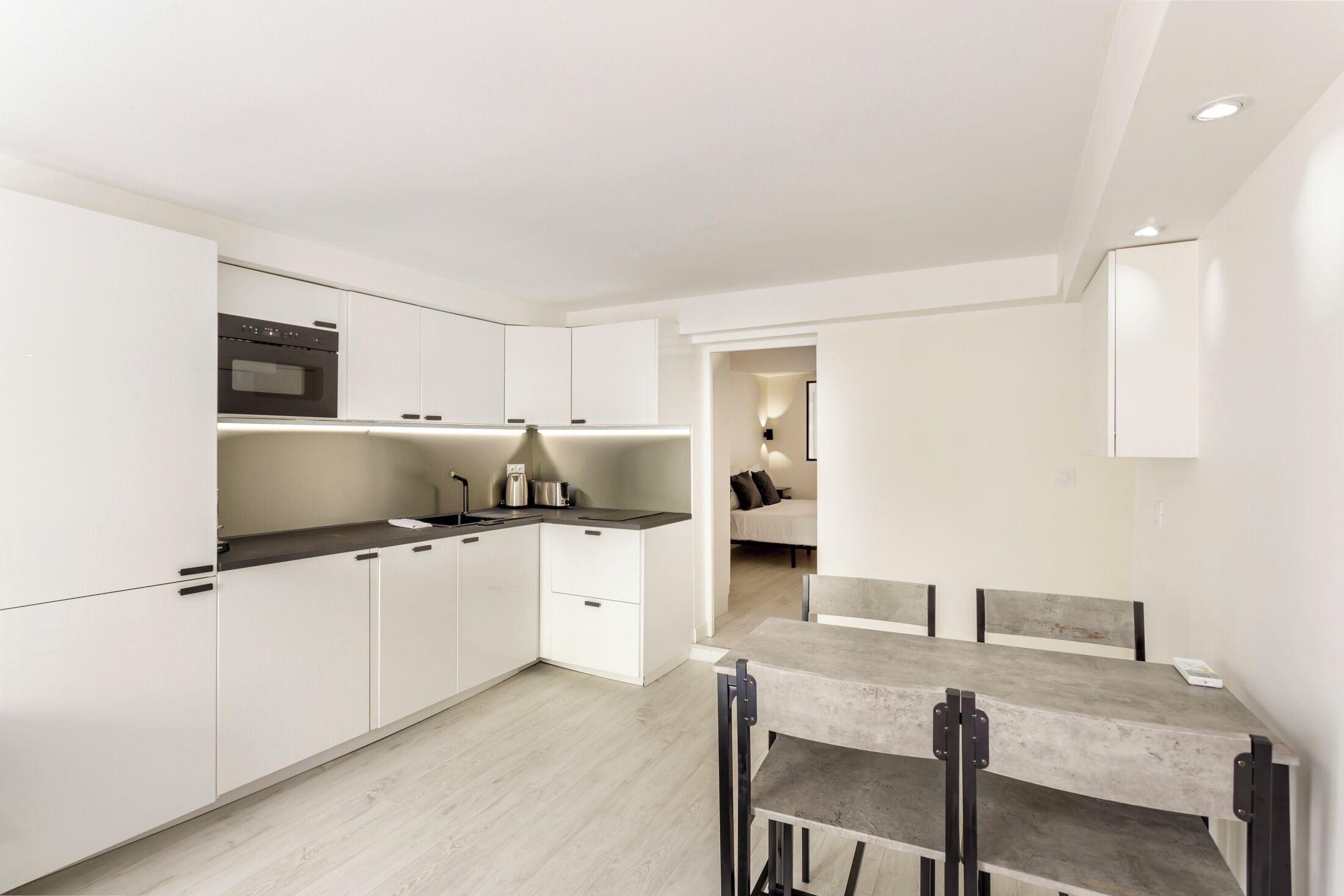A modern kitchen with white cabinets, a black countertop, and a dining area with a table and chairs.