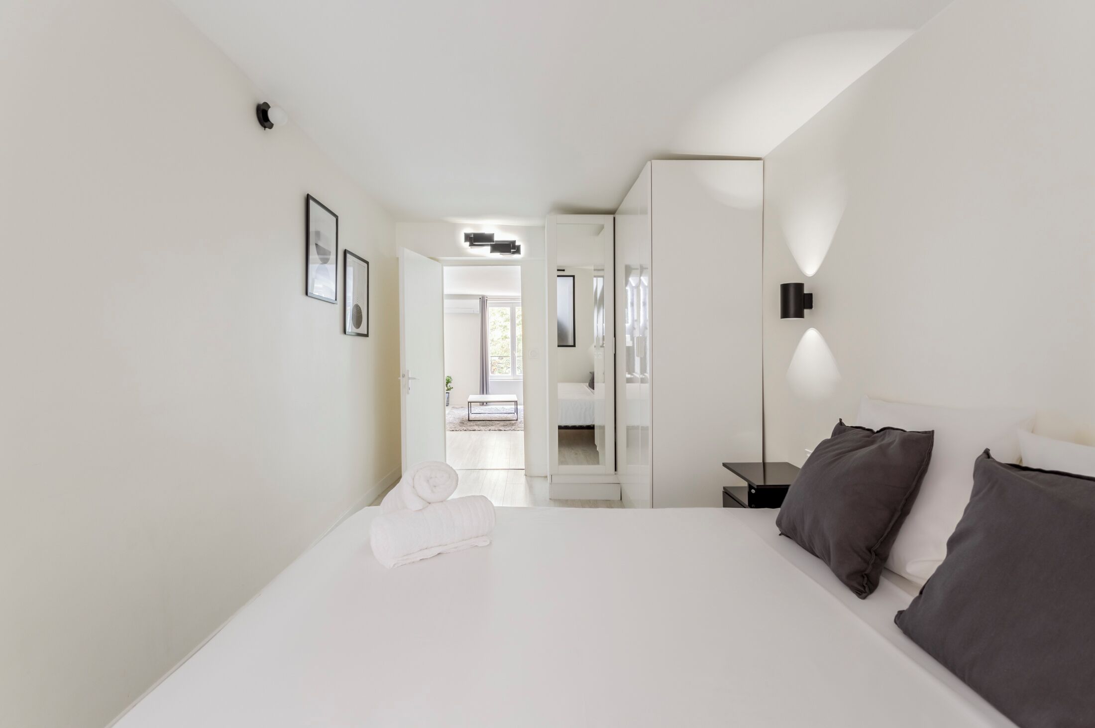Une chambre d’hôtel moderne avec un grand lit, une table de chevet, un miroir et des tableaux encadrés au mur.