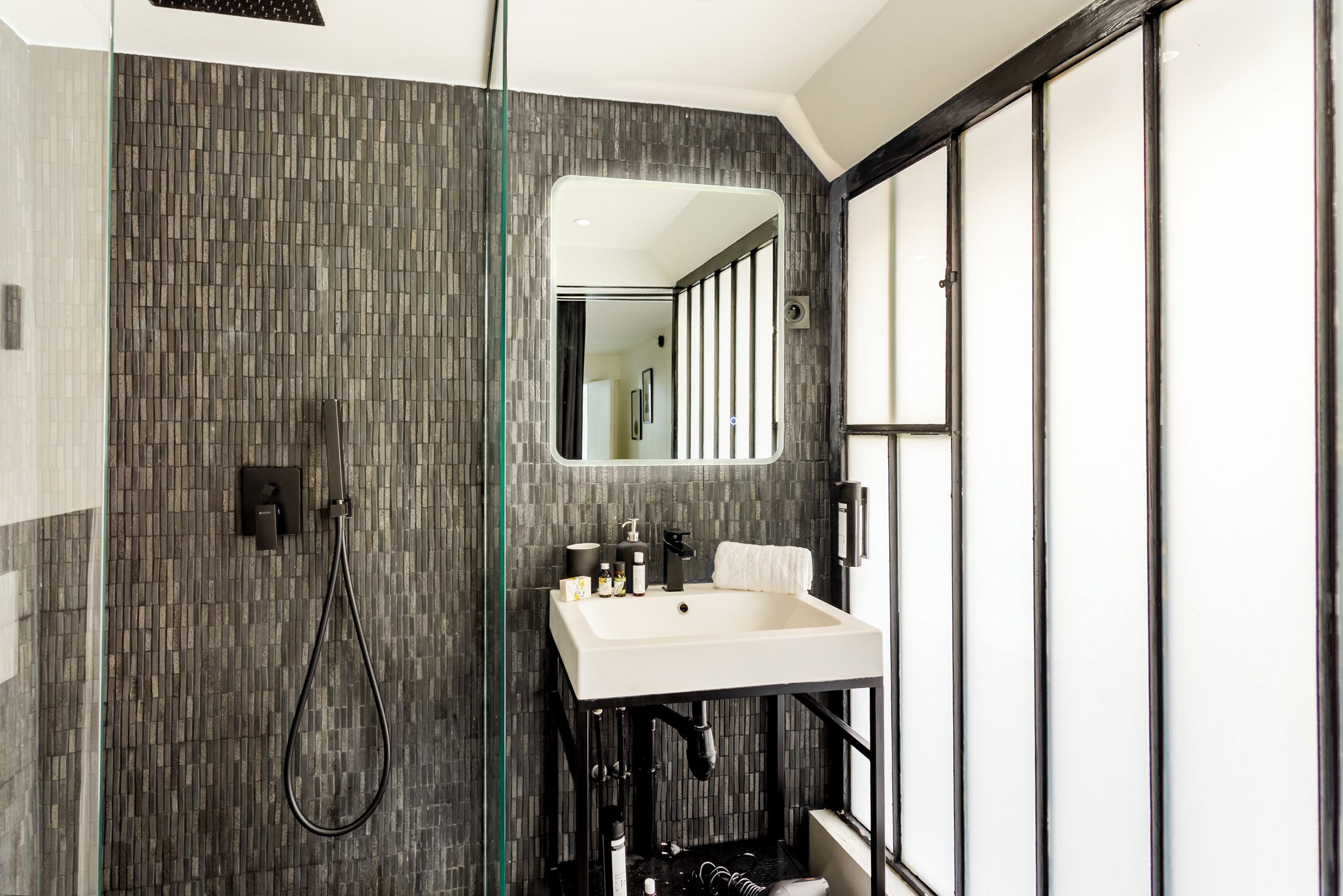 A modern bathroom with a tiled wall, a sink, and a shower.