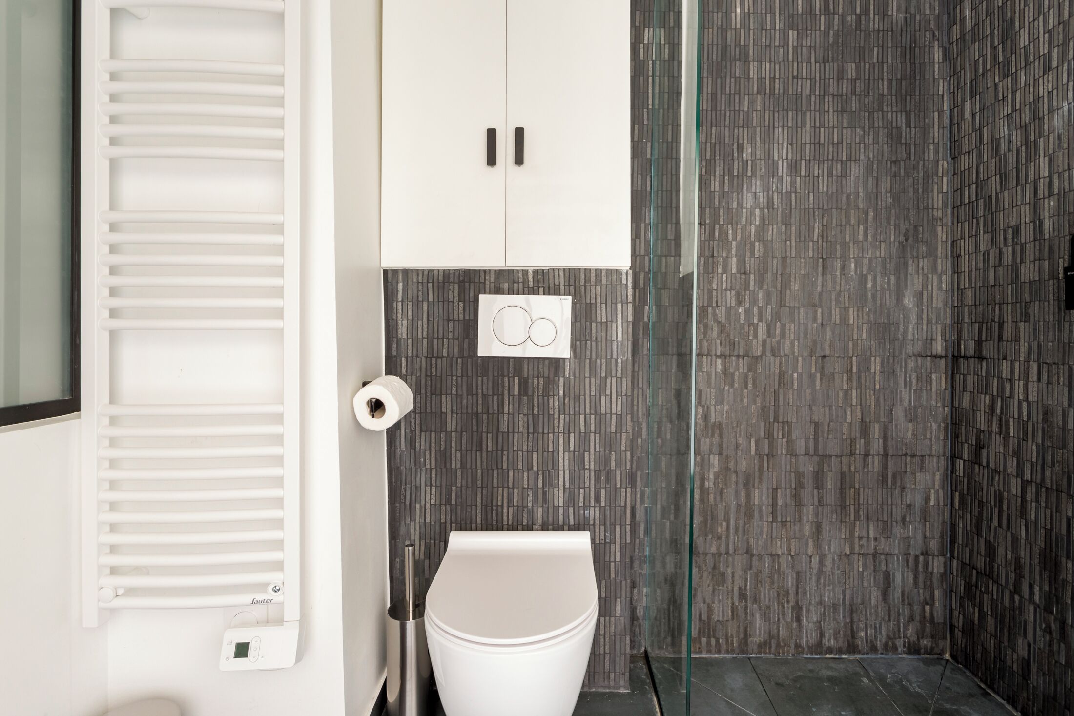 A modern bathroom with a toilet, a glass shower enclosure, and a wall-mounted toilet paper holder.