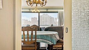 Un espace repas comprenant une table et des chaises, un lustre et une vue sur les bâtiments par une fenêtre.