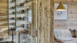A room with a wooden wall, a glass display case with wine bottles, a framed picture, and a sofa. - LUXURY CHALET CLOSE TO THE VILLAGE (Megève)