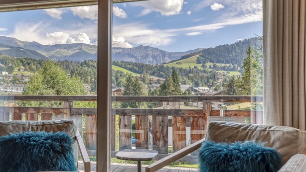 A balcony with a view of mountains and a town. There are two chairs with blue cushions and a small round table. - LUXURY CHALET CLOSE TO THE VILLAGE (Megève)