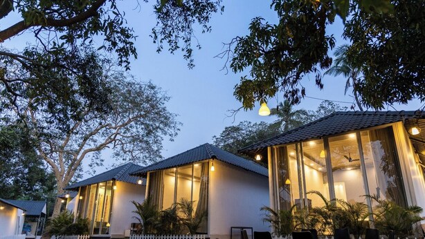 A row of modern, two-story houses with large windows, a white picket fence, and outdoor seating areas. - Natures Cove Resort  (Alibag)