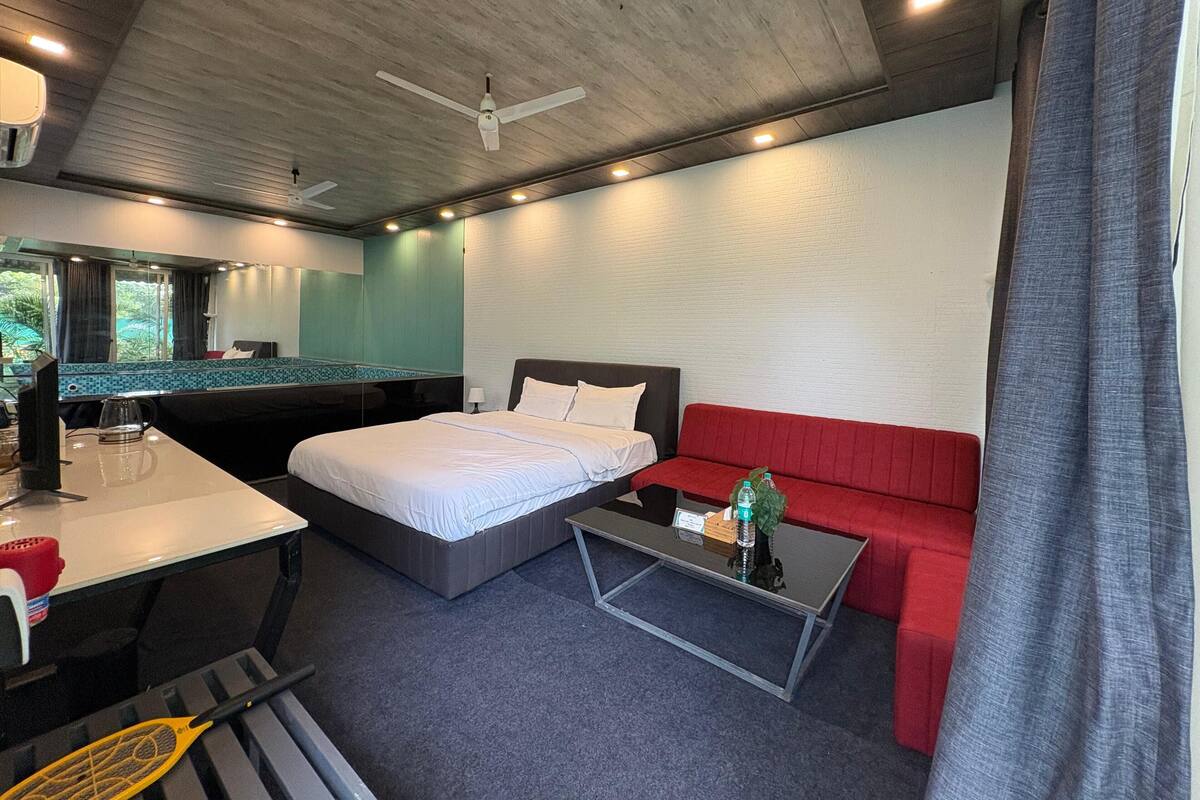 Une chambre d’hôtel moderne avec un lit, un canapé rouge, une petite table, un bureau et un ventilateur de plafond.