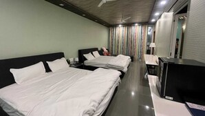 A hotel room with two beds, a desk, a mirror, and a ceiling fan. - Natures Cove Resort  (Alibag)