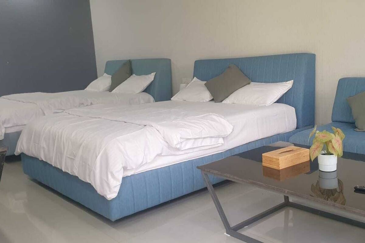 Une chambre d’hôtel moderne avec deux lits, une table basse en verre et un canapé bleu.