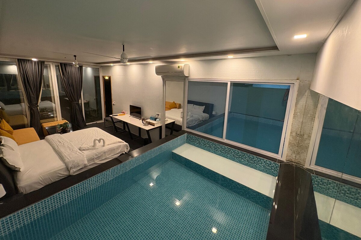 A hotel room with a large window, a bed, a desk, and a small pool area.