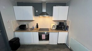 A compact kitchen with white cabinets, a microwave, a toaster, and a sink. - Pine Studio Apartment- Your Own Quiet Space! (Blackpool)