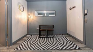 A hallway with a geometric patterned rug, a wall clock, a floor lamp, and a mirror. - Pine Studio Apartment- Your Own Quiet Space! (Blackpool)