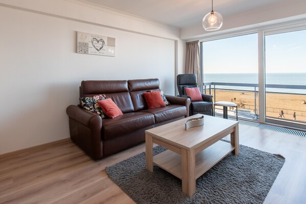 Un salón moderno con un sofá de cuero marrón, una mesa de centro de madera y un ventanal con vistas a la playa.