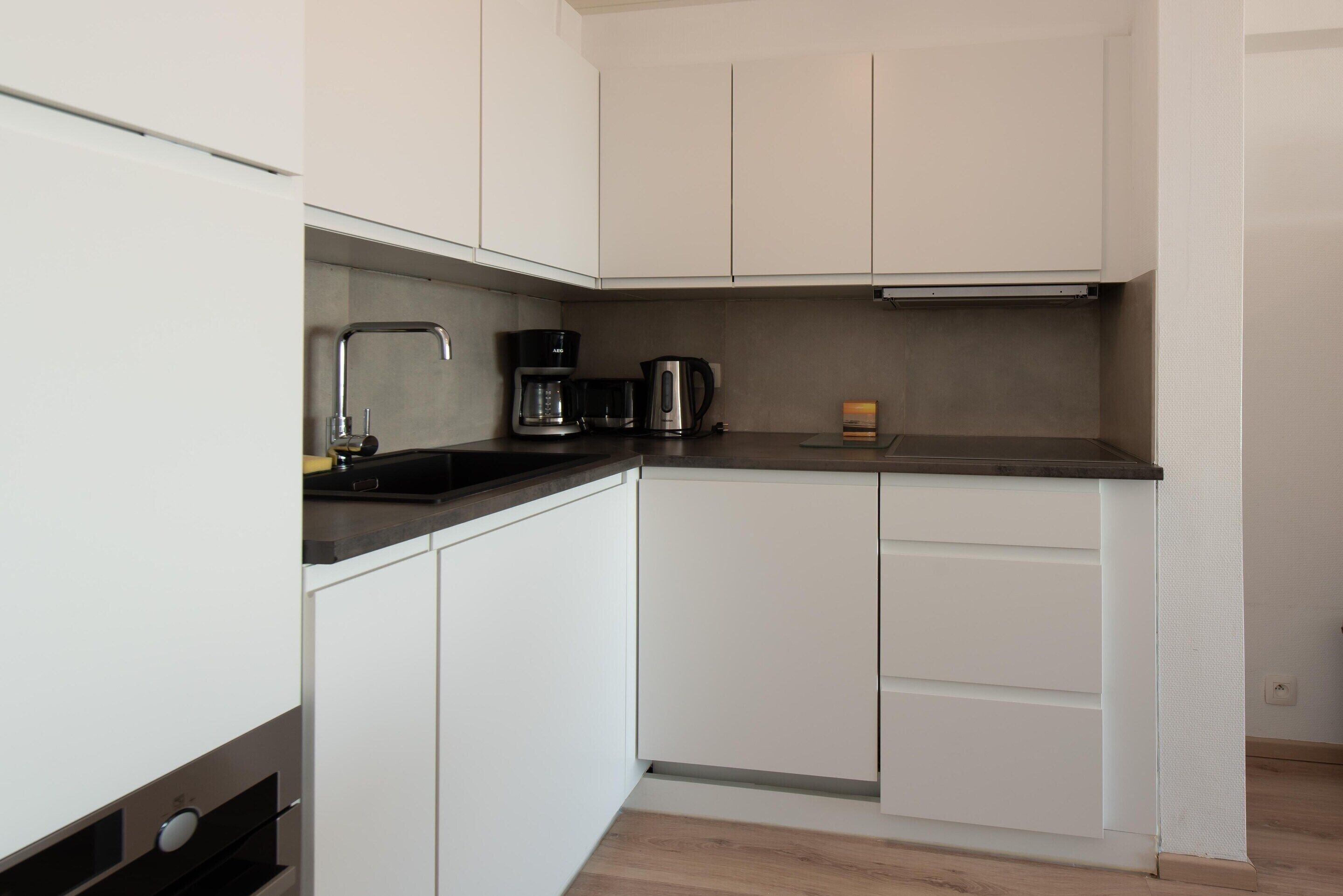 A compact kitchen with white cabinets, a black countertop, and a coffee maker.