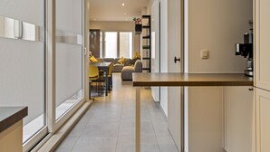 A modern kitchen with a central island, a dining area with yellow chairs, and a living space with a sofa and a coffee machine. - Apartment in Blankenberge Near Sea Dyke (Blankenberge)